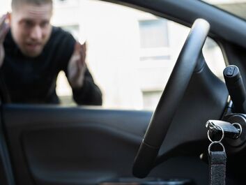 A picture of a man locked out of his car staring at his key in the ignition switch. 