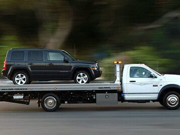 A tow truck hauling an SUV on a flatbed. 